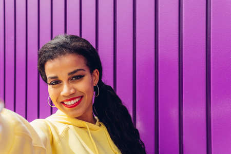 Young influencer taking a selfie portrait on a purple background. Happy girl in yellow clothes and...