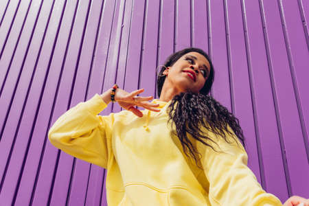 Bottom view of urban dancer in yellow dress on purple background. Low angle shot of a young woman dancing outdoors, urban style and youth fashion concept.の写真素材