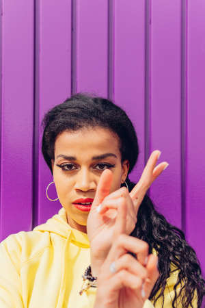 Confident African American female with long black hair gesticulating and looking at camera against purple background on street of cityの写真素材