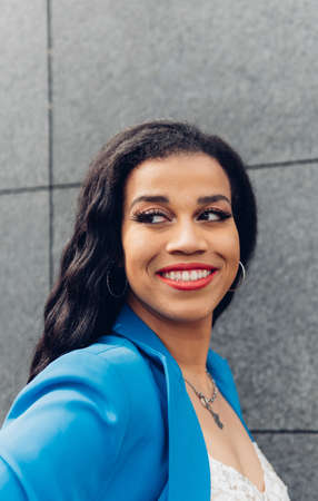 Positive African American female with dark hair smiling and looking at camera while standing on...