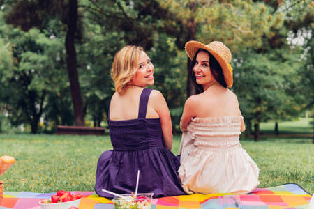 Young adult female friends having a picnic in the countryside smiling at the camera on a summer day. Girls having breakfast in nature on a sunny day. Concept of healthy food, meeting and nature.の写真素材