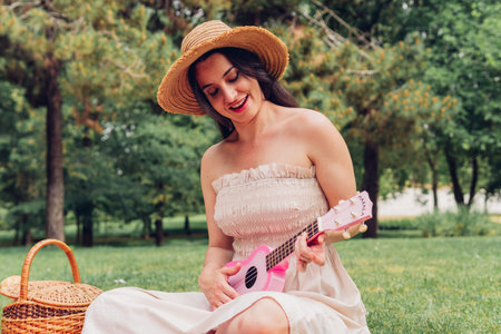 Woman playing the ukulele at a picnic with friends in nature singing a song. Hippie woman playing music with her friends while camping.の写真素材