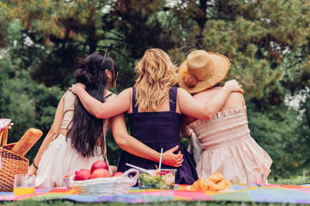 Rear view of a group of unrecognizable female friends, enjoying a picnic with vegan and healthy food outdoors during a trip.の写真素材