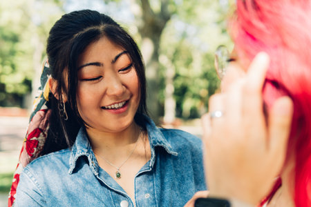 Positive young Asian woman with dyed hair smiling talking to her friend in the park on a sunny dayの写真素材