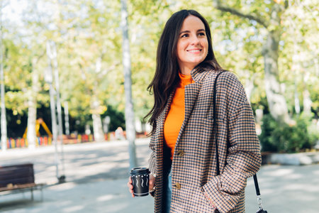 Young elegant woman walking down the street of the city center with a smile and a coffee.の写真素材