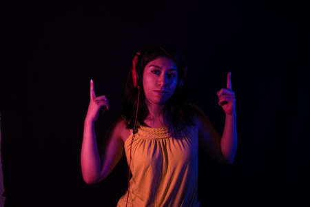 Young woman with headphones listening to music and dancing isolated over dark backgroundの写真素材