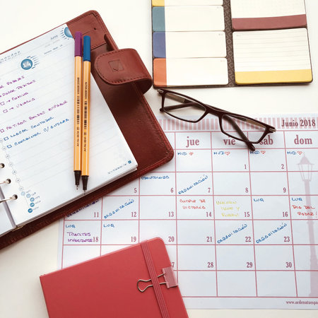 On the desk there are different elements for personal organization and time management, agendas, a writing element, reading glasses and some calendars and self-adhesive notes.の写真素材