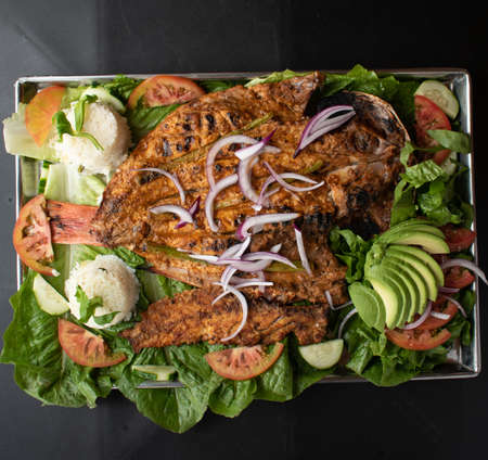 Mexican food, grilled fish, shaken on a salad of lettuce, avocado, tomato and onionの写真素材