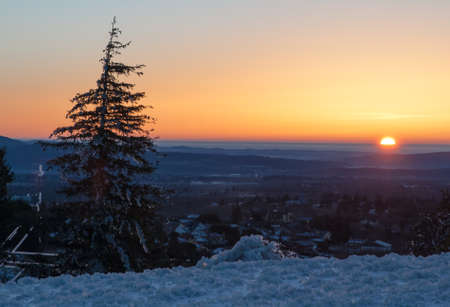 Snowy landscape in the mountains at sunrise with trees and the Sun in the backgroundの写真素材