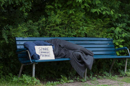 Homeless man on a park bench with a carboard sign