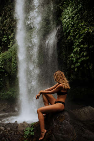 a girl poses in a bikini in a waterfall in a forest in baliの写真素材
