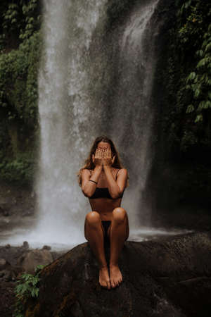 a girl poses in a bikini in a waterfall in a forest in baliの写真素材