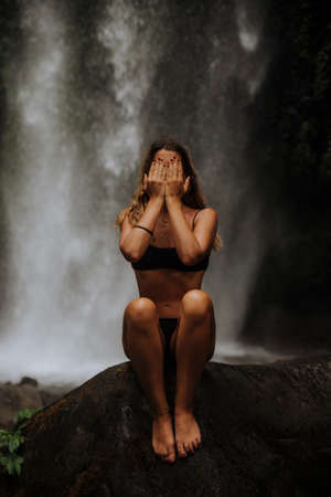 a girl poses in a bikini in a waterfall in a forest in baliの写真素材