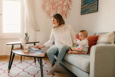young business mother works from home with her laptop, with her baby by her side having funの写真素材