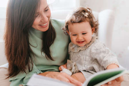little girl having fun sitting on her pregnant mother in the roomの写真素材