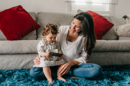 young pretty mother plays with her daughter on the living room floor with the phoneの写真素材