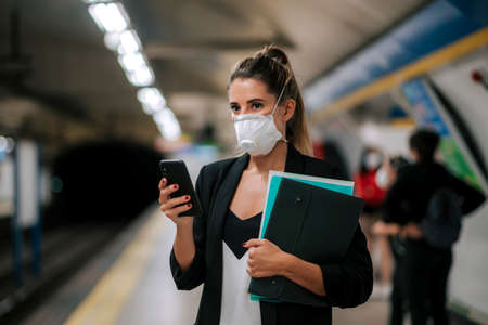 young woman with medical mask in the subway uses her phoneの写真素材