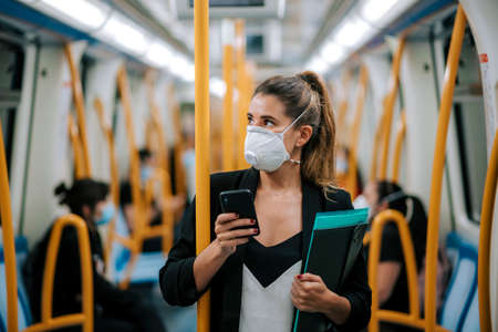 young woman with medical mask in the subway uses her phoneの写真素材
