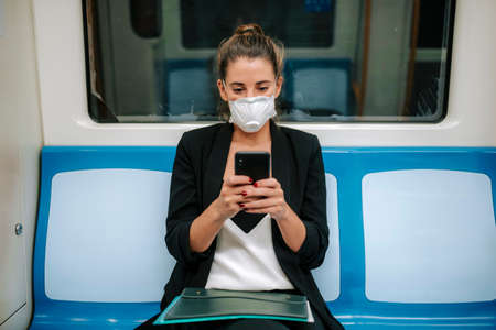 young woman with medical mask in the subway uses her phoneの写真素材