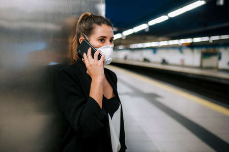 young woman with medical mask in the subway uses her phoneの写真素材