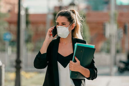 young business woman goes to work talking on the phone with medical maskの写真素材
