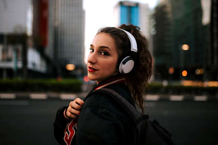 Beautiful spanish woman listening to music with earphones and smart phone outdoors. Latin girl in sport clothes with curly hairstyle in urban background.の写真素材