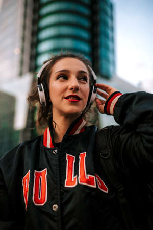 Beautiful spanish woman listening to music with earphones and smart phone outdoors. Latin girl in sport clothes with curly hairstyle in urban background.の写真素材
