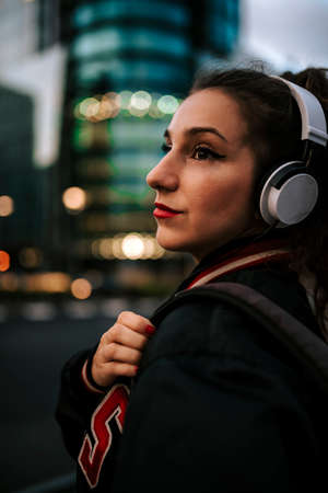 Beautiful spanish woman listening to music with earphones and smart phone outdoors. Latin girl in sport clothes with curly hairstyle in urban background.の写真素材