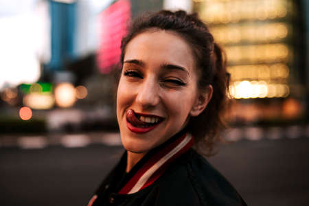 Beautiful spanish woman listening to music with earphones and smart phone outdoors. Latin girl in sport clothes with curly hairstyle in urban background. night cityの写真素材