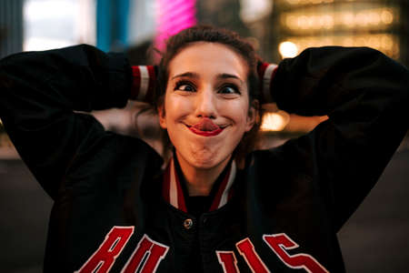 Beautiful spanish woman listening to music with earphones and smart phone outdoors. Latin girl in sport clothes with curly hairstyle in urban background. night cityの写真素材