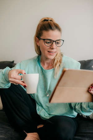 Happy beautiful woman watching videos or enjoying entertainment content on a tablet sitting on the...