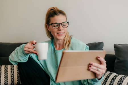 Happy beautiful woman watching videos or enjoying entertainment content on a tablet sitting on the...
