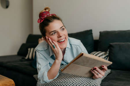 Happy beautiful woman watching videos or enjoying entertainment content on a tablet sitting on the...