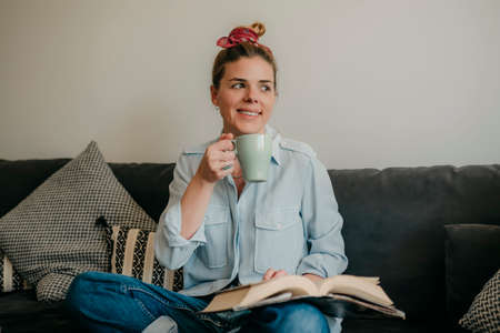 Beautiful smiling woman reading a book and lying on the sofa in the living room. Have a good time at home.の写真素材