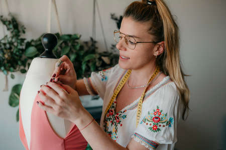 Young woman fashion designer measuring mannequin, seamstress holding tape working with dummy in cozy...