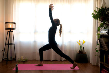 Beautiful blonde woman doing home workout indoors. Woman practice yoga at home. Fit girl using workout tutorials for healthy active lifestyle. Woman using quarantine for home workouts. Stretching in homeの写真素材