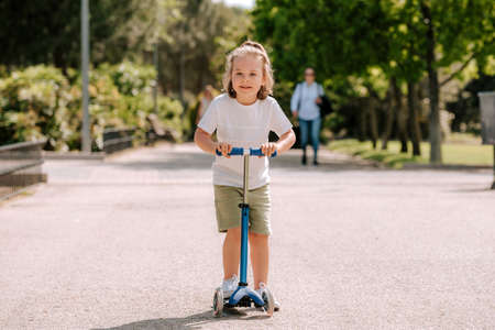 Boy learn to ride scooter in a park on sunny summer day. Preschooler boy riding a roller. Kids play...