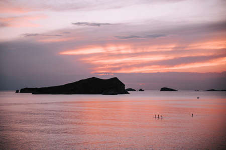 beautiful colors at sunset in ibiza on the sea. People doing paddle surf with a nice imageの写真素材