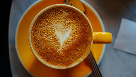 A hear formed with milk in an orange cup of coffeeの写真素材