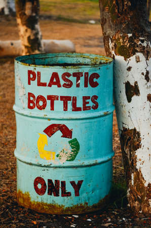 A recyle sign with hand painted letters. the bin is light blue and the painted letters are red. The bin is in the woods against a tree.の写真素材