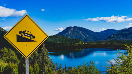 A mirror lake in Patagonia with a car going down a hill sign.の写真素材