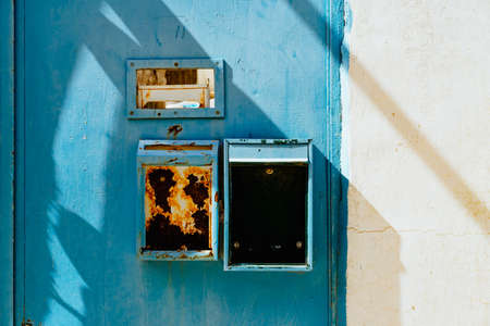 Rusty mailboxes and a mail slot on a blue door next to a white wall.