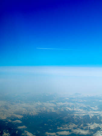 Aeroplane flying through clear blue sky over the Swiss Alps with vapour trailの写真素材