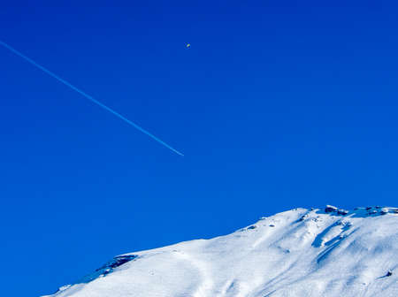 Aeroplane flying above a mountain with vapour trails and para-sailerの写真素材