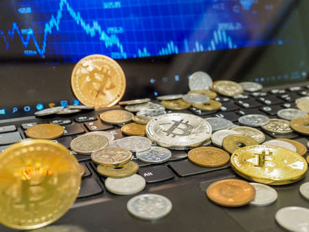 Bitcoin and currency coins scattered on computer keyboard with exchange charts of crypto currency on...