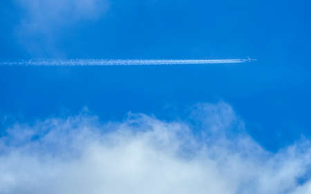 A jet flies across a blue cloudy sky leaving vapour trailsの写真素材