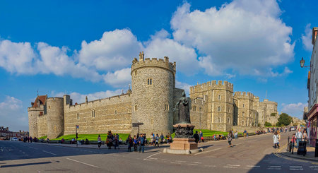WINDSOR, UK - APRIL 7, 2015: A panoramic view of Windsor Castle and the Queen Victoria statue on a sunny day. Tourists can be seen walking along the street outside the historic royal residence in Berkshire.のeditorial素材