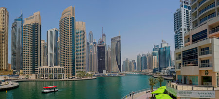 DUBAI, UAE - APRIL 7, 2013: A panoramic daytime view of the Dubai Marina canal. A red water taxi can be seen navigating the waterway, surrounded by modern high-rise residential skyscrapers and the waterfront promenade.のeditorial素材