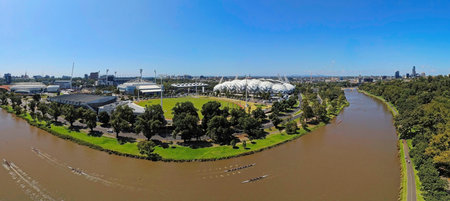 A wide aerial panoramic view of the Yarra River winding past the Melbourne & Olympic Parks sporting precinct. The scene features the stadium, tennis centre, MCG and rowing teams training on the water on a sunny day.の写真素材