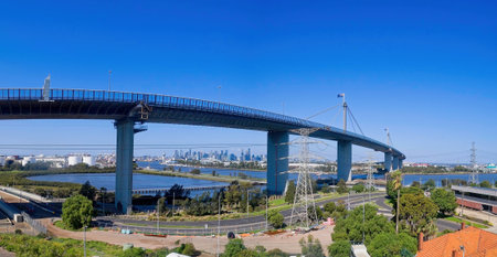A panoramic side view of the massive concrete pylons and span of the West Gate Bridge in Melbourne. The shot highlights the engineering structure crossing the river, with the city skyline visible through the bridge supports.の写真素材